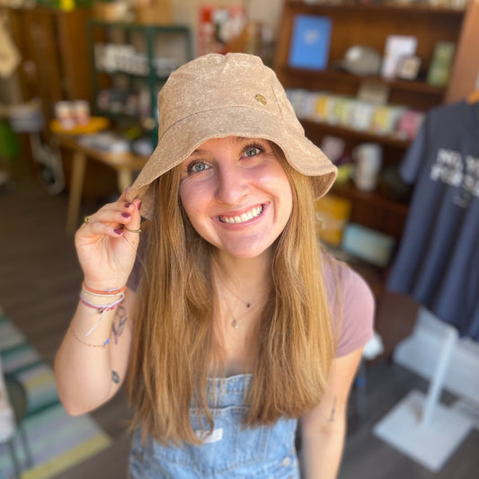 Jordan poses in our terry cloth bucket hat in a light brown. She is looking up at the camera and smiling.